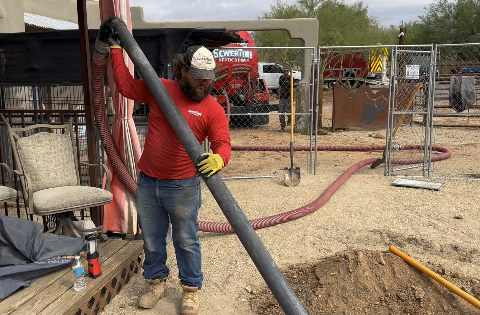 SewerTime technician in red shirt pumping a septic tank at a residential property