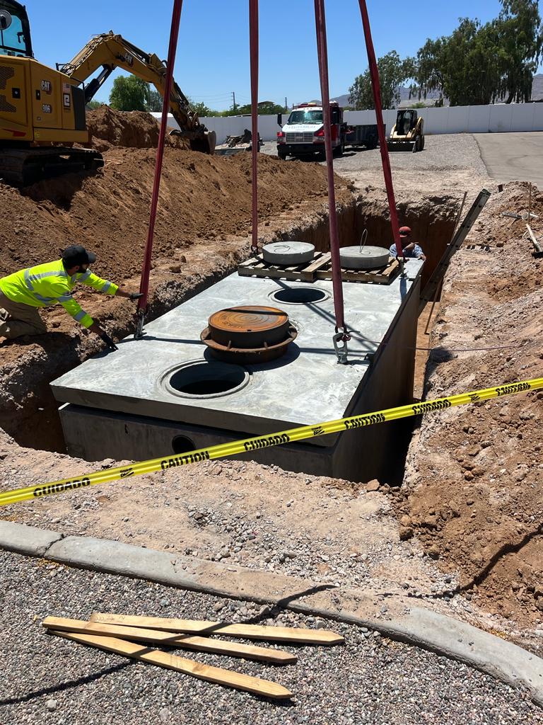 Concrete septic tank being lowered into excavated site with crane rigging