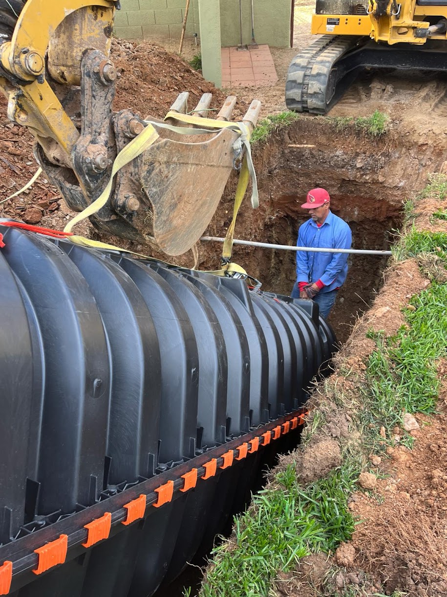 Plastic septic tank being placed into excavated trench with excavator
